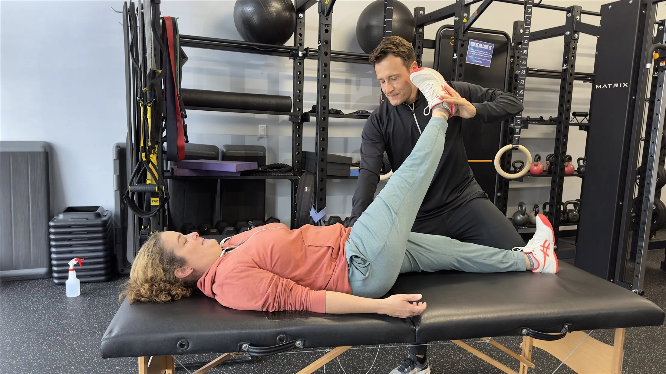 Dario guiding a client through an assisted hamstring stretch on the training table