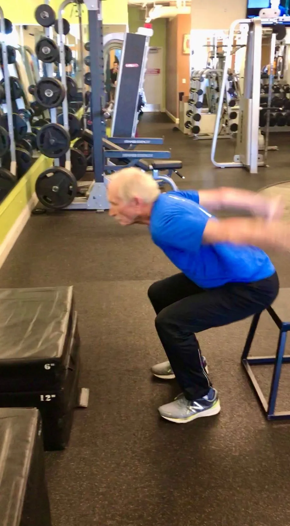 A senior client driving through box squats at the gym