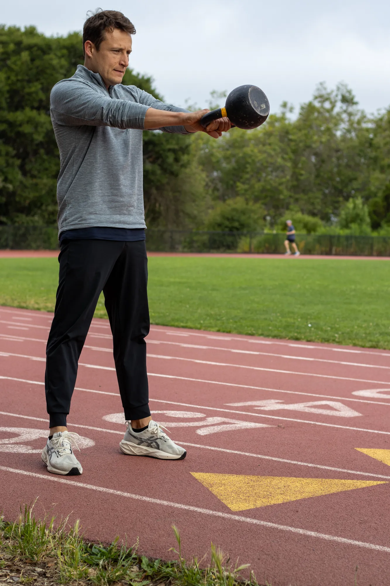 Dario coaching a kettlebell swing outdoors at the track
